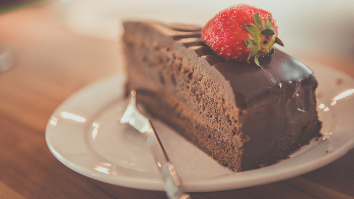 A slice of chocolate cale topped with a strawberry on a white plate