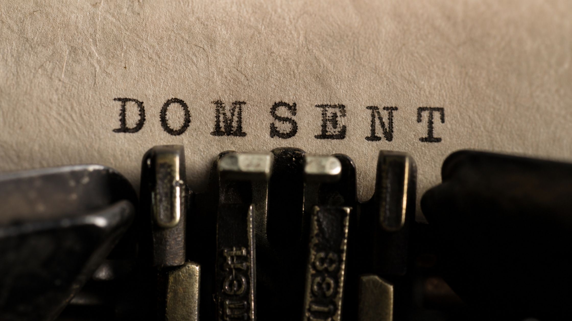 A close-up of a vintage typewriter typing the word ‘DOMSENT’ on paper, with the title ‘Guest Post: Introducing Domsent, Mistress Claudia Sky’ displayed across the bottom in white text.