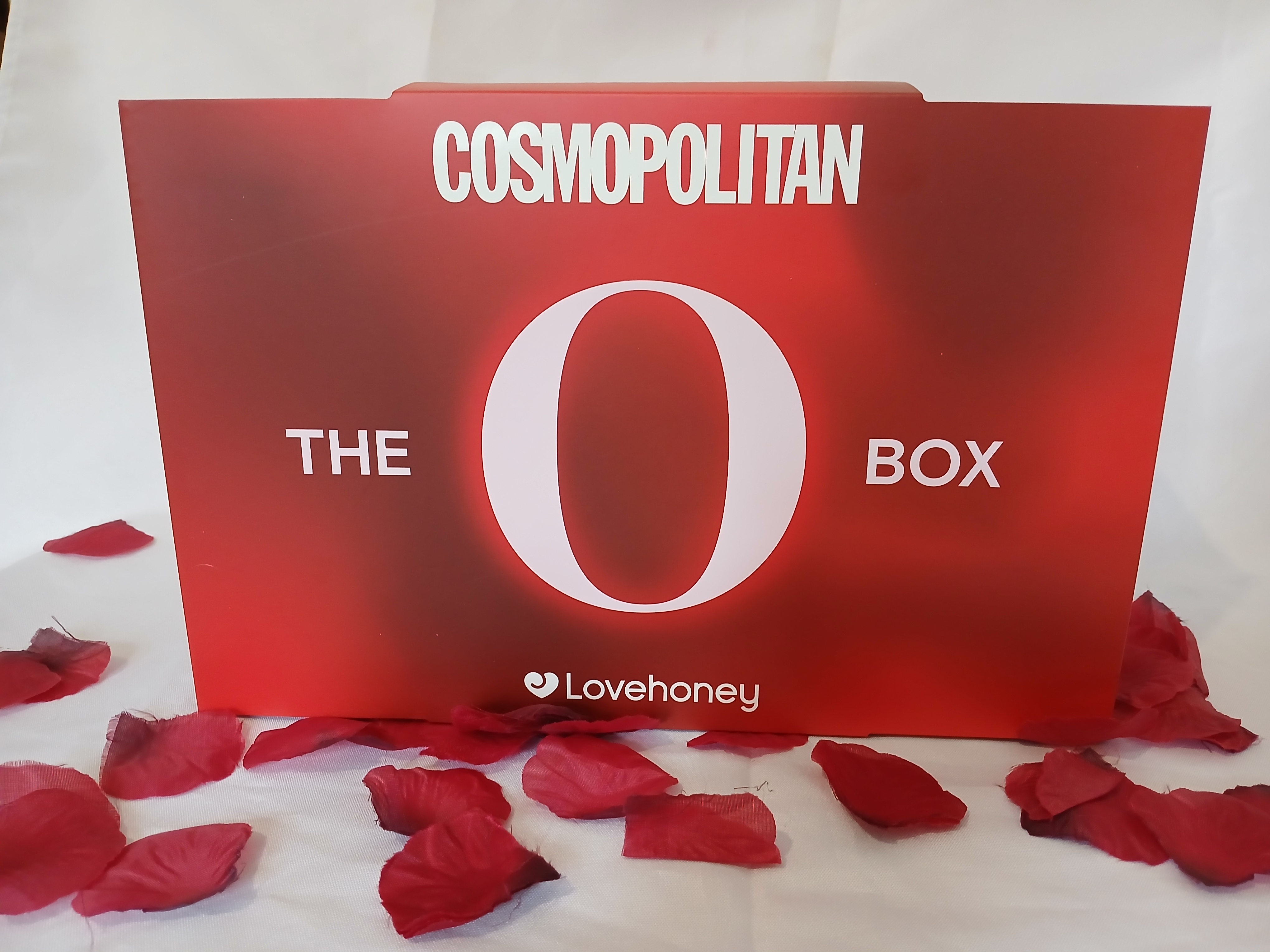 Cosmopolitan O Box on a white sheet and red rose petals